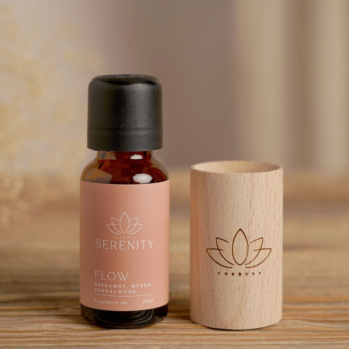 Flow Lotus Wood Block Diffuser with an amber glass oil bottle labelled "Serenity Flow," the natural wood cylinder engraved with a lotus motif, set on a wooden surface.