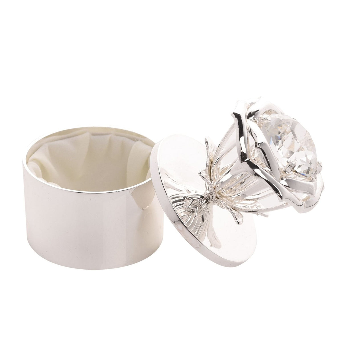 Round silver metal trinket box with a rose and leaf design lid featuring a large clear faceted jewel centre, shown open with a cream fabric lining, on a white background.