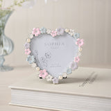 Heart-shaped metal photo frame with daisy flowers in pink, lilac, blue and white and pearl beads, holding a 4 x 3.5in print, displayed on a book beside a vase.