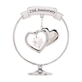 Chrome circle decoration on a round pedestal base, featuring a "25th Anniversary" ribbon banner above two overlapping silver hearts with a clear crystal drop, set against a plain white background.