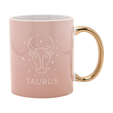 Pink stoneware mug with a gold handle, featuring a white line-art Taurus bull head, stars, and "TAURUS" text, shown on a plain white background.
