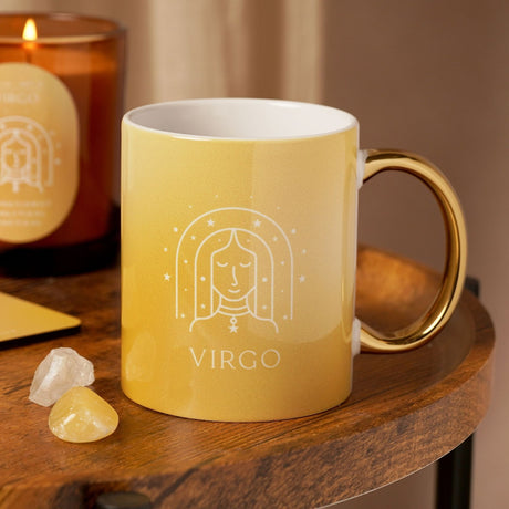 Yellow stoneware Virgo mug with gold handle, featuring a white line illustration of a serene face under a starry arch and "VIRGO" text, shown on a wooden table beside crystals and a candle.