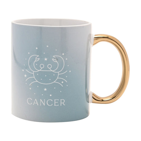 Pale blue stoneware mug with glossy gold oval handle, featuring a white line-drawn Cancer crab symbol, stars, and "CANCER" text, shown on a plain white background.