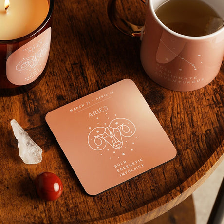 Square wooden coaster in gloss pink with white Aries ram line art, star details, and "Bold Energetic Impulsive" text, shown on a wooden table beside a mug and candle.