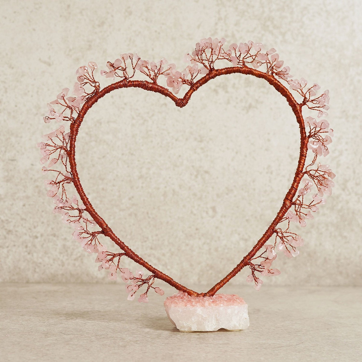 Rose Quartz Heart Tree Figurine with copper-toned wire branches tipped with pink rose quartz chips, mounted on a white crystal base against a plain light background.