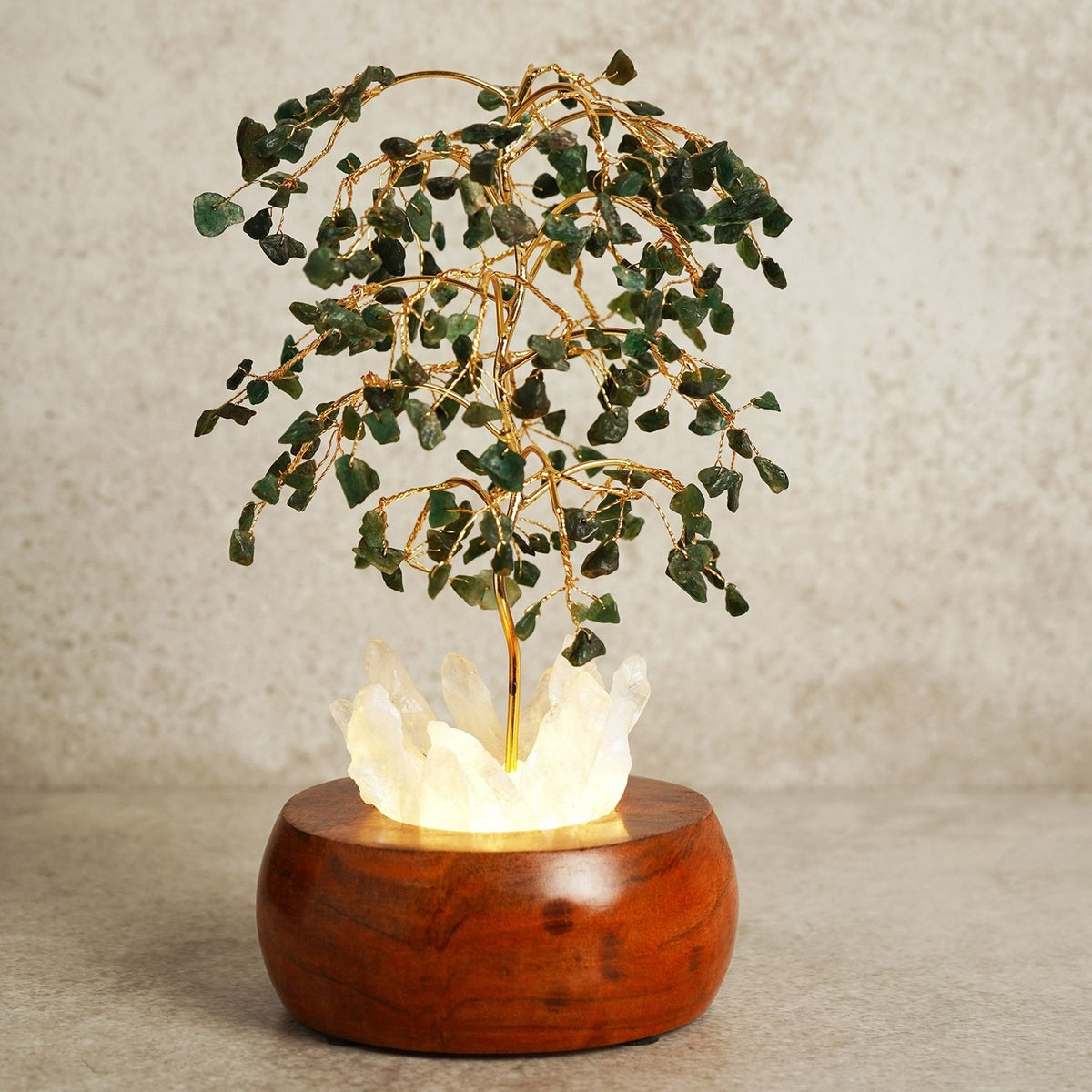 Aventurine LED Glow Tree decoration with gold wire branches holding green chip leaves over a glowing crystal cluster set in a rounded brown wooden base, shown against a plain light background.