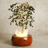 Aventurine LED Glow Tree decoration with gold wire branches holding green chip leaves over a glowing crystal cluster set in a rounded brown wooden base, shown against a plain light background.