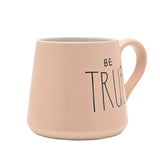 Pink tapered earthenware mug with "BE TRUE" printed in black lettering, white interior, and a sandy clay band at the base, shown on a plain white background.