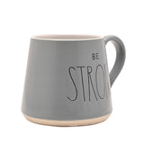Grey tapered earthenware mug with "BE STRONG" in black lettering, white interior and pale foot band, shown on a plain white background.