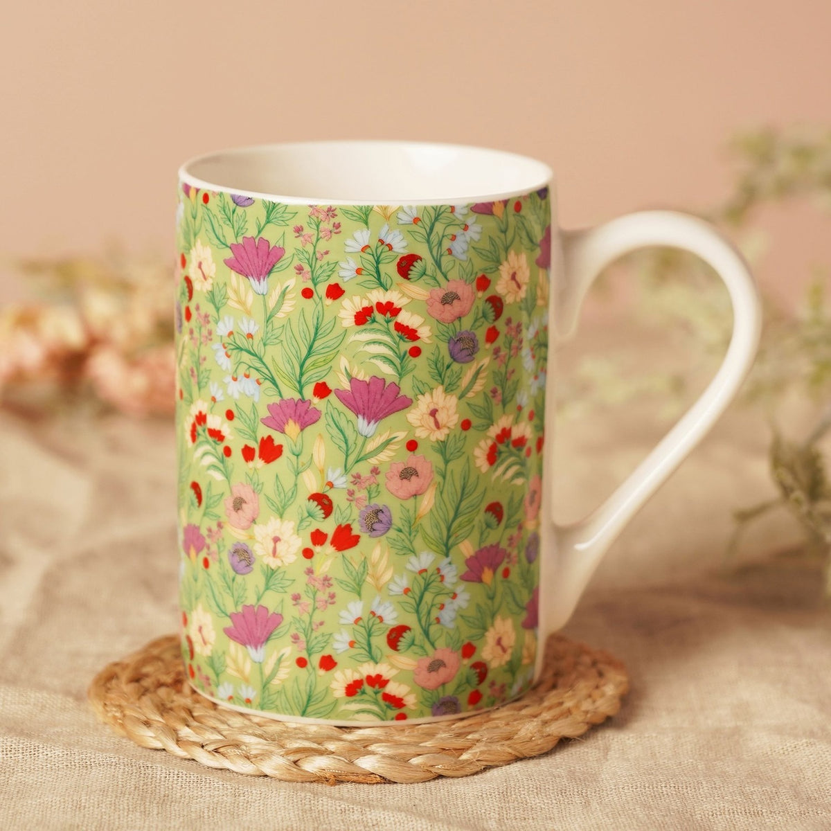 Floral Print Porcelain Mug 10oz in green with cream handle, rim and interior, shown on a woven coaster against a soft pink background.