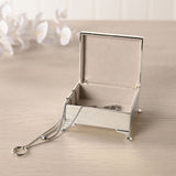Open silverplated rectangular trinket box with four feet, polished silver finish and lined interior, holding a necklace, shown on a light surface with flowers behind.
