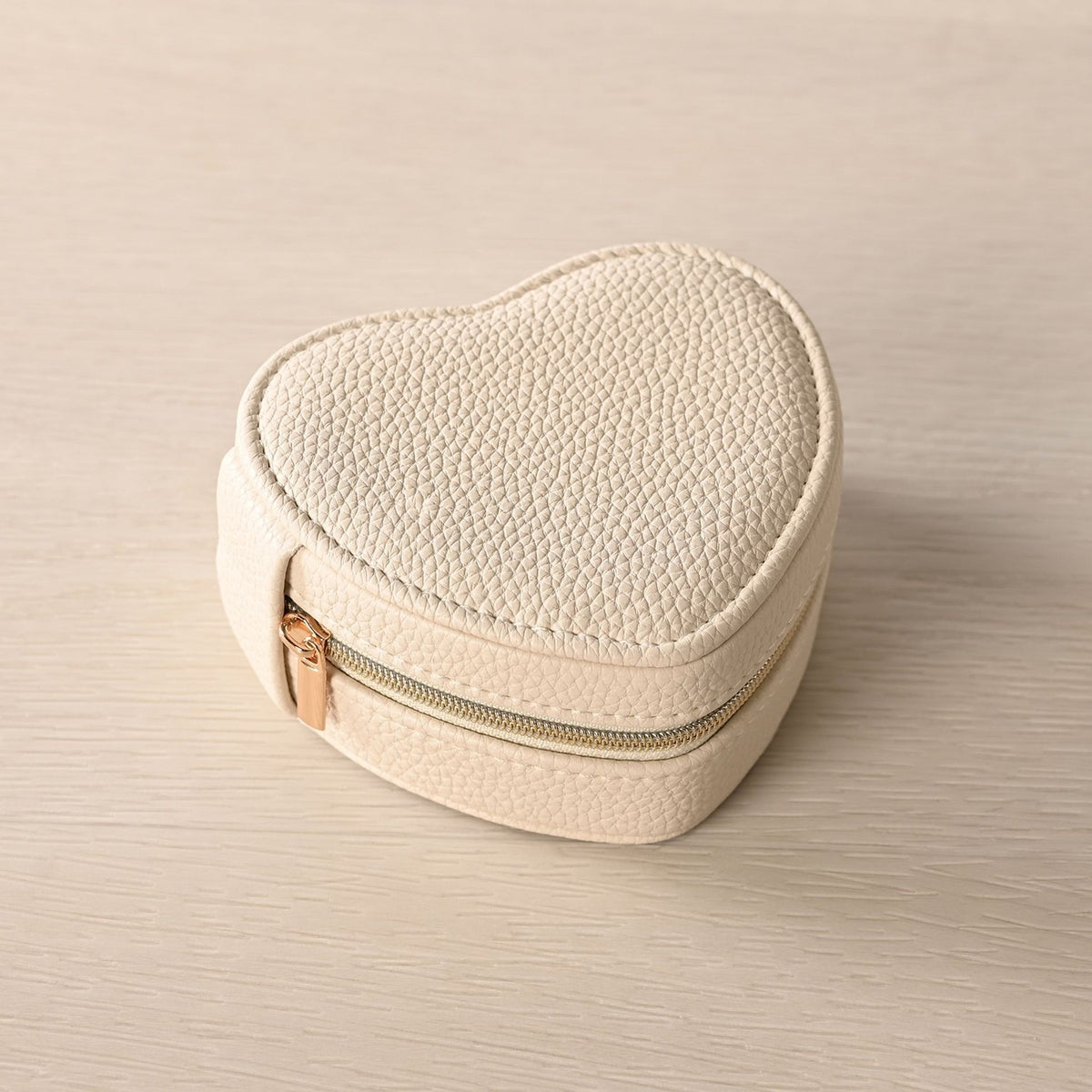 Heart-shaped jewellery box in cream plastic with pebble-grain texture and gold-tone zip closure, shown on a plain light background.