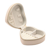 Open heart-shaped jewellery box in cream pebble-grain plastic with gold-tone zip, showing a ring roll strip, divided compartments, and soft interior lining on a white background.