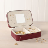 Medium rectangular jewellery box in red pebbled plastic with gold-tone zip, open to show a cream-lined interior with ring rolls, earring holes, a lid mirror, and jewellery displayed alongside.