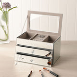 Rectangular 2 drawer mirror glass jewellery box in silver, lid open to show a lined tray with ring roll, holding rings and a necklace on a dressing table.