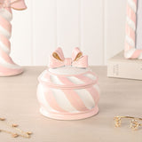 Round Candy Cane Bow Resin Trinket Box, 12cm, with pink and white spiral stripes and a gold-lined pink bow lid, shown on a table beside jewellery.