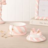 Round Candy Cane Bow Resin Trinket Box, 12cm, with pink and white striped base and gold-accented bow lid, shown open beside jewellery on a tabletop setting.