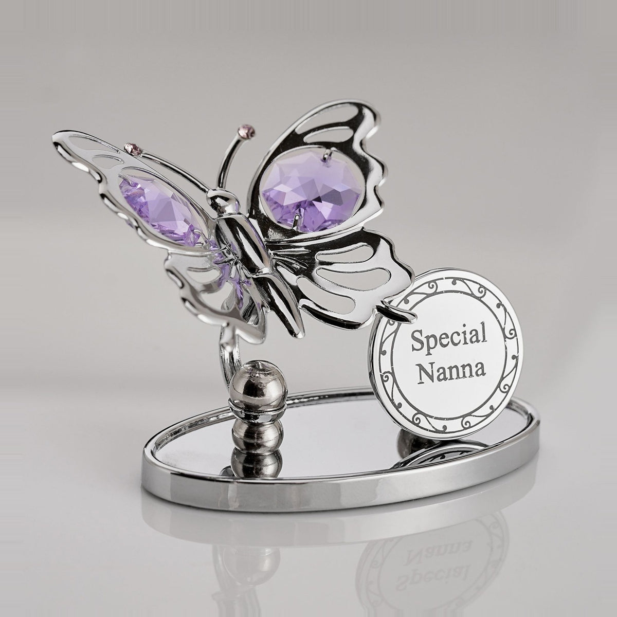 Chrome-plated metal butterfly plaque with violet crystal wings and antennae, beside a round "Special Nanna" disc, set on an oval mirrored base against a plain light background.