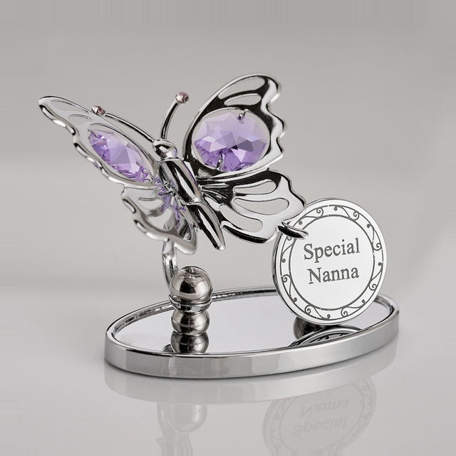 Chrome-plated metal butterfly plaque with violet crystal wings and antennae, beside a round "Special Nanna" disc, set on an oval mirrored base against a plain light background.
