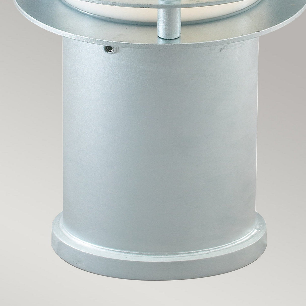 A close-up of the Stockholm Small Bollard - Silver reveals its cylindrical metallic form in a modern design, characterized by a smooth surface and a small hole near the top. Made from galvanized steel, it belongs to a larger structure with the top partially visible against a neutral background.