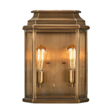 The St Martins 2 Light Outdoor Large Wall Light in aged brass exudes historical charm, featuring two exposed Edison bulbs within a rectangular frame of brass and glass.