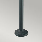 A close-up image of the base of a dark-colored vertical metal pole standing on a plain, light gray background. The Stockholm 2 Light Twin Lamp Post - Black boasts a cylindrical pole and a slightly elevated circular base, reflecting Scandinavian-inspired design principles.