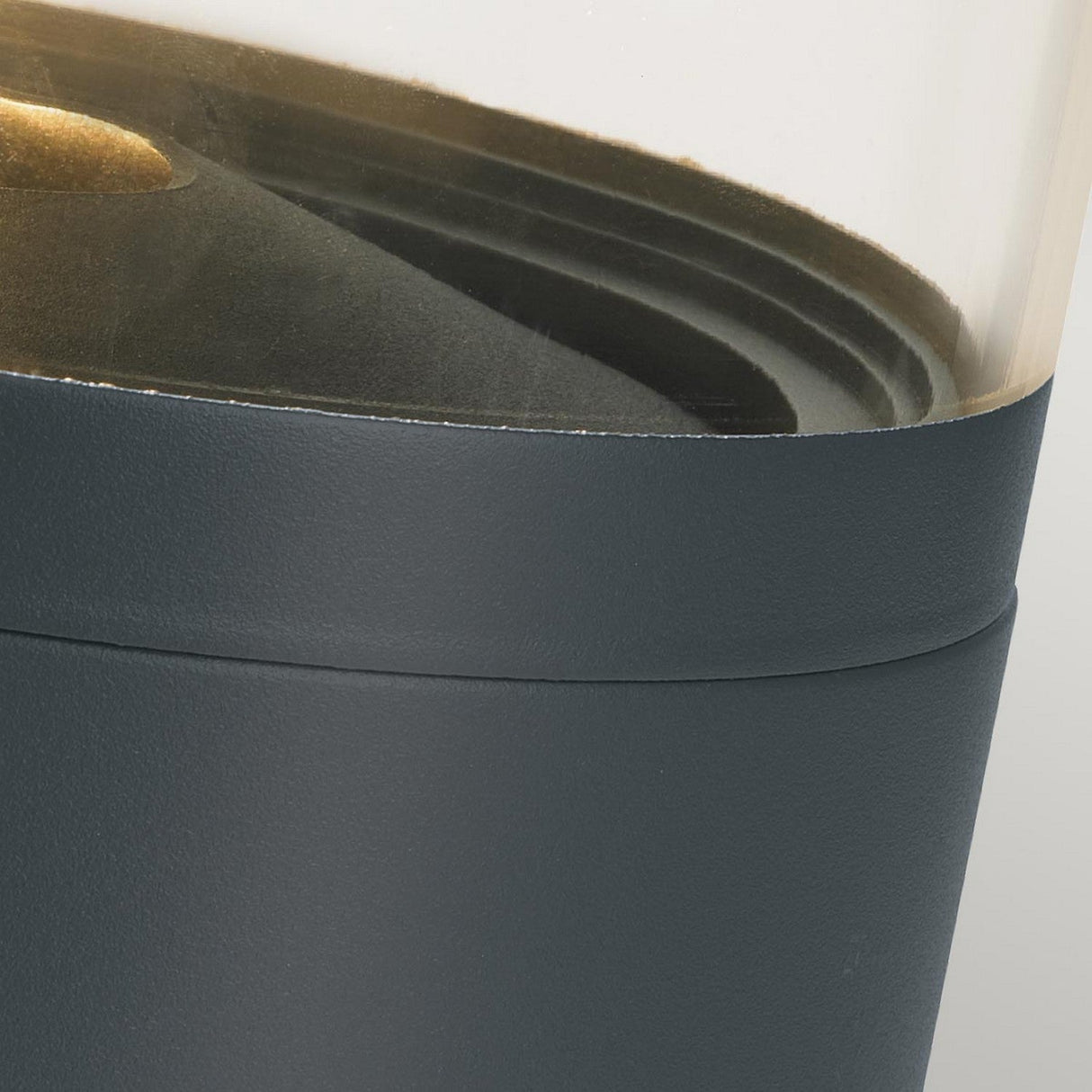 Close-up image of the Stavanger LED Small Bollard in Graphite, featuring a transparent container with a dark base, perfect for outdoor lighting. Inside, layered black elements capture attention. Its modern design is vandal-resistant and seamlessly integrates the transparent top with the solid dark bottom—ideal for this LED Small Bollard setup.