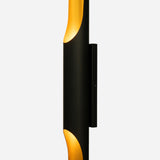 The Stealth 2 Light Wall Light in Gold & Black is a modern black sconce with an elongated cylindrical shape and a glowing gold interior. It emits light from openings at the top and bottom, which enhances its sleek and contemporary design.