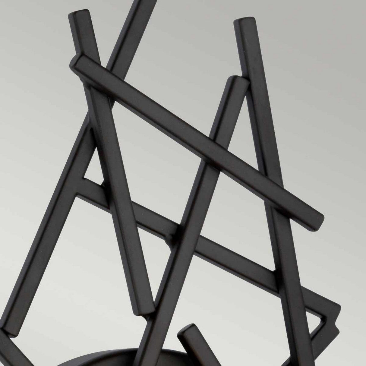 The abstract sculpture features intersecting black metal rods creating a geometric, angular pattern against a simple background. Its dynamic design suggests artistic expression, reminiscent of the interplay of light and shadow cast by the Taiko 1 Light Wall Light in Olde Bronze.