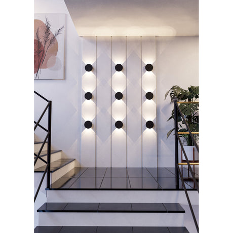 Talamello LED Wall Light 15cm in black, round aluminium disc fixtures arranged in rows on a staircase wall, each casting warm white light above and below.