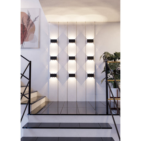 Talamello LED Wall Light 20cm in black, shown in multiple rows on a staircase wall, casting warm white up and down light in a modern stairwell setting.