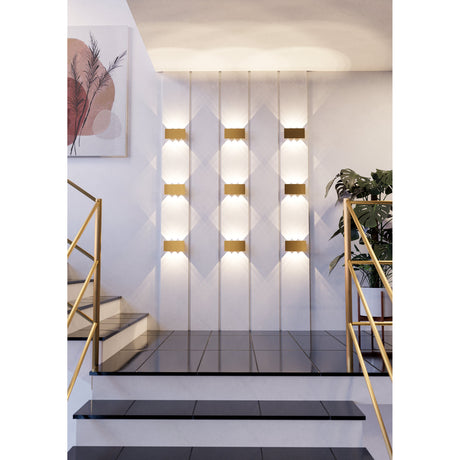 Talamello LED Wall Light 20cm in brushed gold, shown in a staircase setting with multiple units mounted in vertical rows casting warm up-and-down light on white panelled walls.