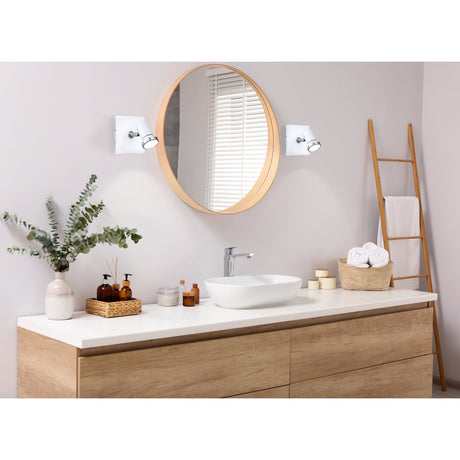 Tamara 1 wall spotlight in white and chrome, square backplate with adjustable head, shown mounted either side of a round mirror above a bathroom vanity.