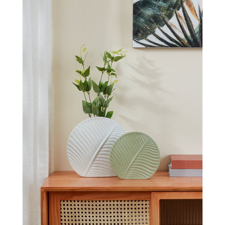 Tanabe Ceramic Vase in light green, a round, flat disc-shaped vase with raised leaf-vein relief, matt earthenware finish, shown on a wooden sideboard beside a matching white version.