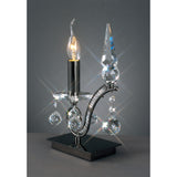 The Tara 1 Light Crystal Table Lamp - Black Chrome showcases a candle-shaped bulb, hanging crystal accents, and a pointed finial on a reflective base, ideal for adding elegant decorative lighting to your space.