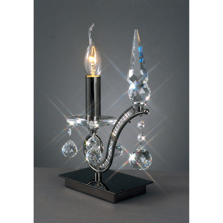 The Tara 1 Light Crystal Table Lamp - Black Chrome showcases a candle-shaped bulb, hanging crystal accents, and a pointed finial on a reflective base, ideal for adding elegant decorative lighting to your space.
