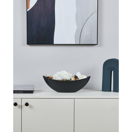 Tazeyol Planter 13cm in black, a long boat-shaped bowl with pointed ends, shown filled with white flowers on a sideboard beneath framed wall art.