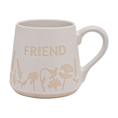 White glazed earthenware mug with tapered body, "FRIEND" lettering, wildflower silhouette border, rounded handle and speckled base, shown on a plain background.