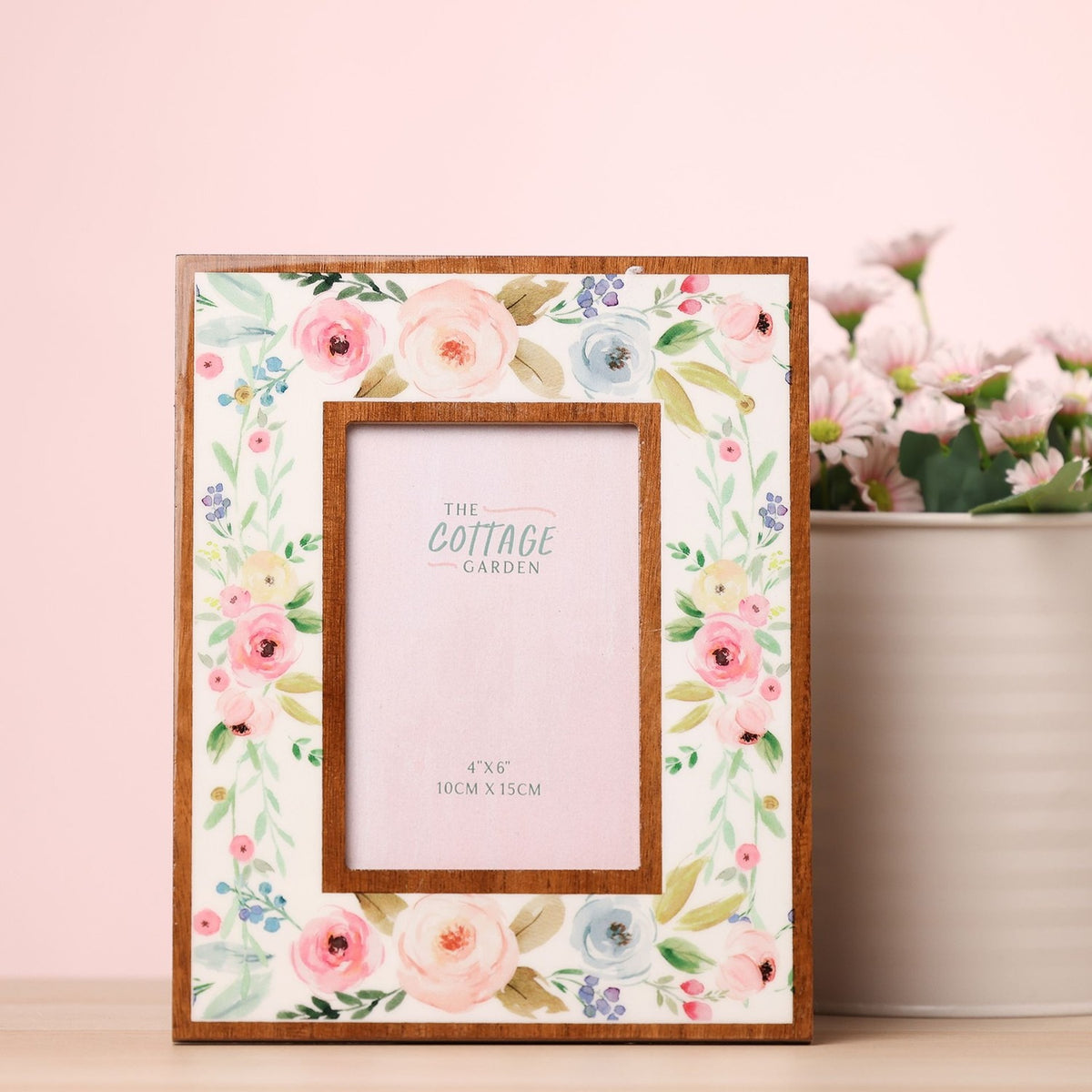 Rectangular wooden photo frame for a 6 x 4in photo, white face with pastel pink, peach and blue floral print and warm wood inner border, shown on a table beside flowers.