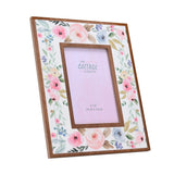 Wooden photo frame for a 4x6in picture, with a white face painted in pastel pink, blue and sage floral patterns and a raised warm wood inner border, shown at an angle on a white background.
