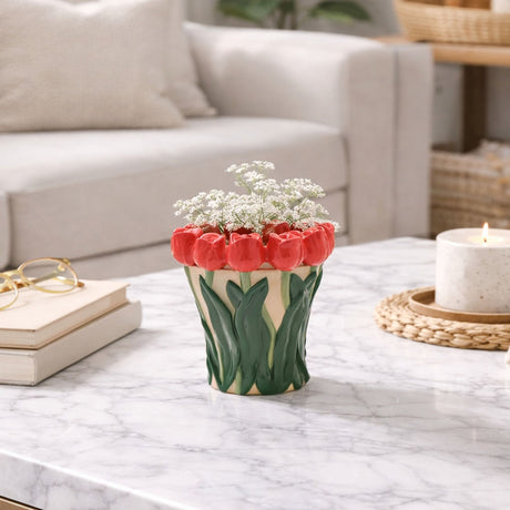 Tulip Rim hand painted ceramic vase with raised red tulip heads and green leaf relief on a peach-cream ground, holding white flowers on a marble coffee table.