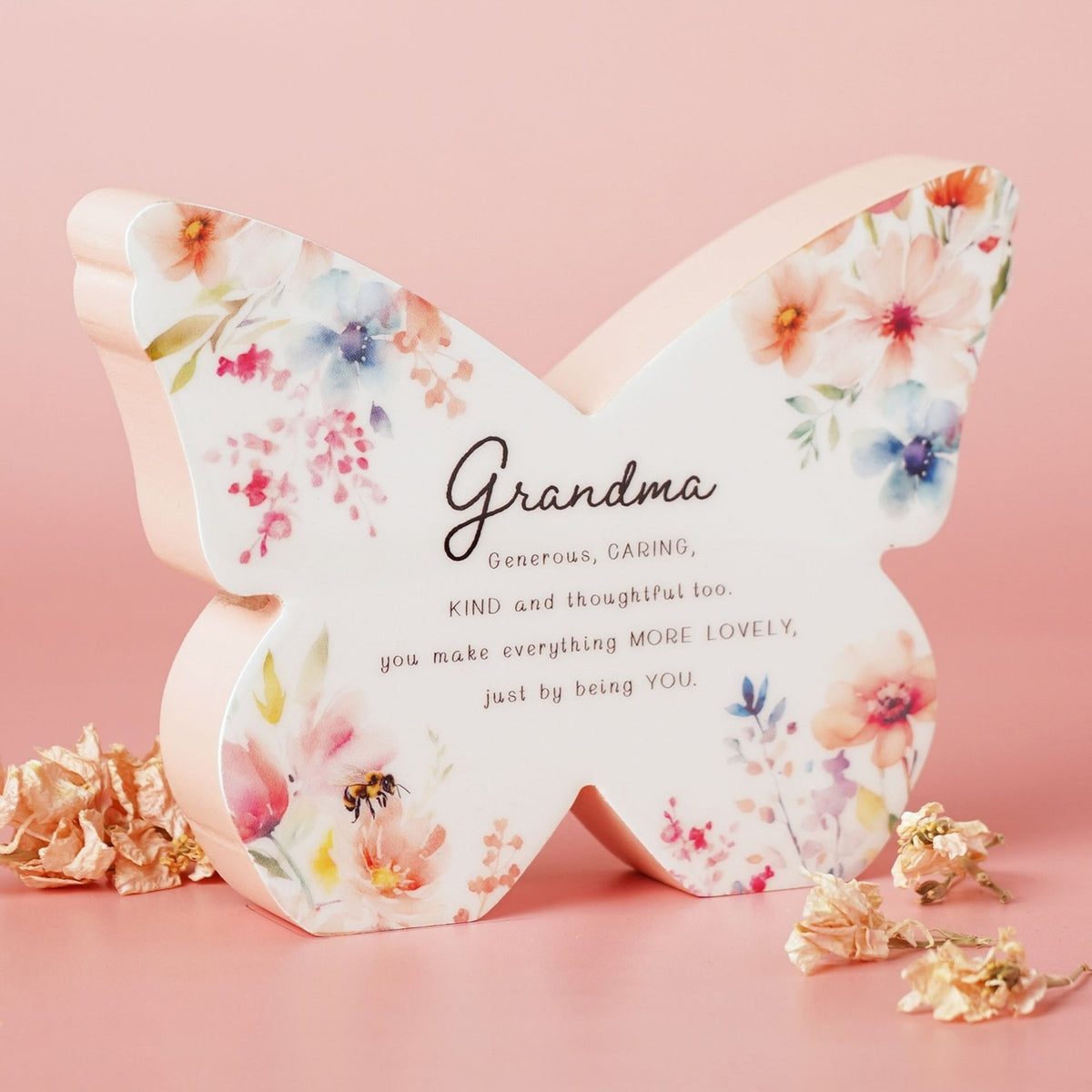 Wooden butterfly mantel decoration in white and pink, printed with pastel floral watercolour pattern and a "Grandma" verse, set against a pink background.