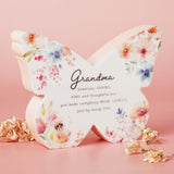 Wooden butterfly mantel decoration in white and pink, printed with pastel floral watercolour pattern and a "Grandma" verse, set against a pink background.