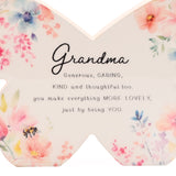 Wooden butterfly mantel decoration with a glossy white finish, printed with pastel pink, peach and blue watercolour flowers and a small bee, featuring the sentimental "Grandma" verse in script text.