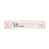 Skinny white wooden wall plaque with watercolour floral sprays in pink, coral and lilac at each end, reading "Mum, Never forget how LOVED you are" in black script, shown on a plain background.