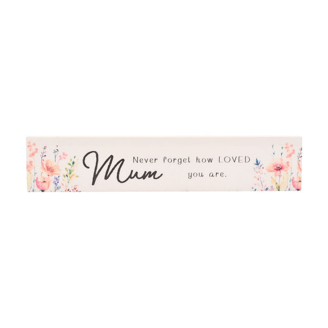 Skinny white wooden wall plaque with watercolour floral sprays in pink, coral and lilac at each end, reading "Mum, Never forget how LOVED you are" in black script, shown on a plain background.