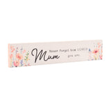 Slim white wooden wall plaque reading Mum, Never forget how LOVED you are in black script, with pink, coral and lilac watercolour floral sprays at each end and a pink edge detail.