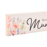 Close-up of a slim white wooden wall plaque with pink edges, reading "Mum" in black script, bordered by watercolour floral prints in coral and lilac tones.