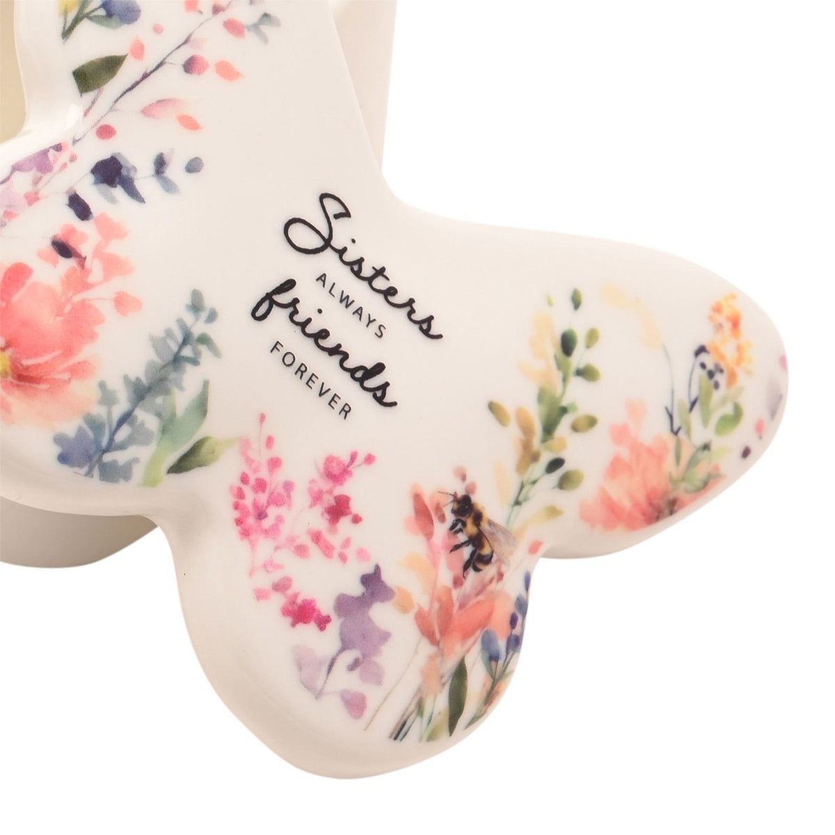 Close-up of the white glass butterfly trinket box lid, showing watercolour garden flowers, a small bee, and "Sisters ALWAYS friends FOREVER" in black script.