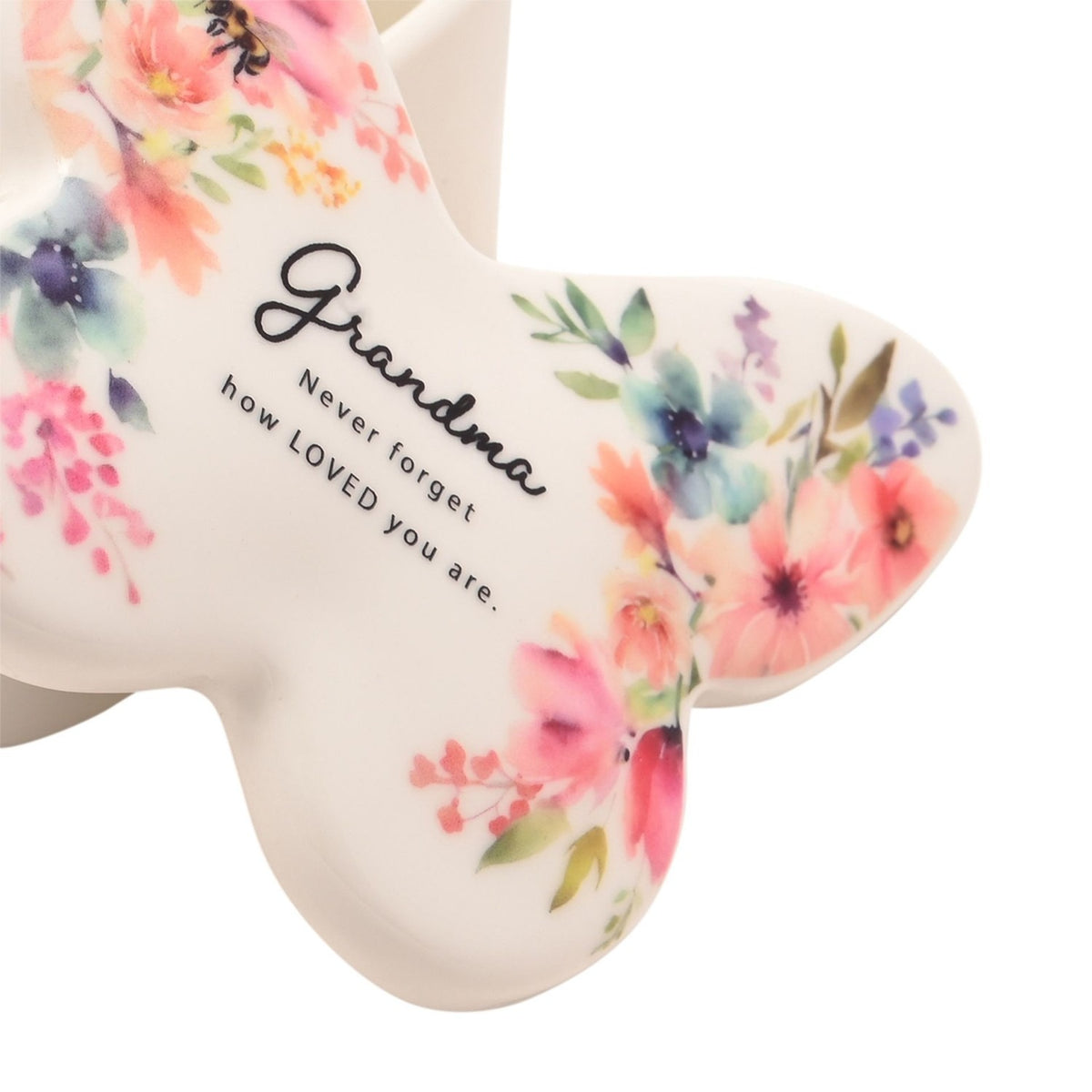 Close-up of white glass butterfly-shaped trinket box lid with pink, coral and blue watercolour floral design, reading "Grandma, Never forget how LOVED you are" in script text.